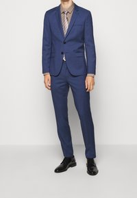 Blue suit with a notched lapel, single button closure, and matching pants. Paired with a light brown shirt and striped tie. Black shoes.