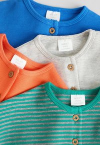 Tre babytröjor: en blå strukturerad tröja, en orange ribbad tröja med träknappar och en grå randig tröja med grön krage.