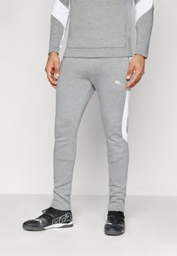 Grå træningsbukser med hvide sidelofar, der har en slim fit, blød tekstur og et lille logo på fronten af hoften. Sæt sammen med sorte sportssko.