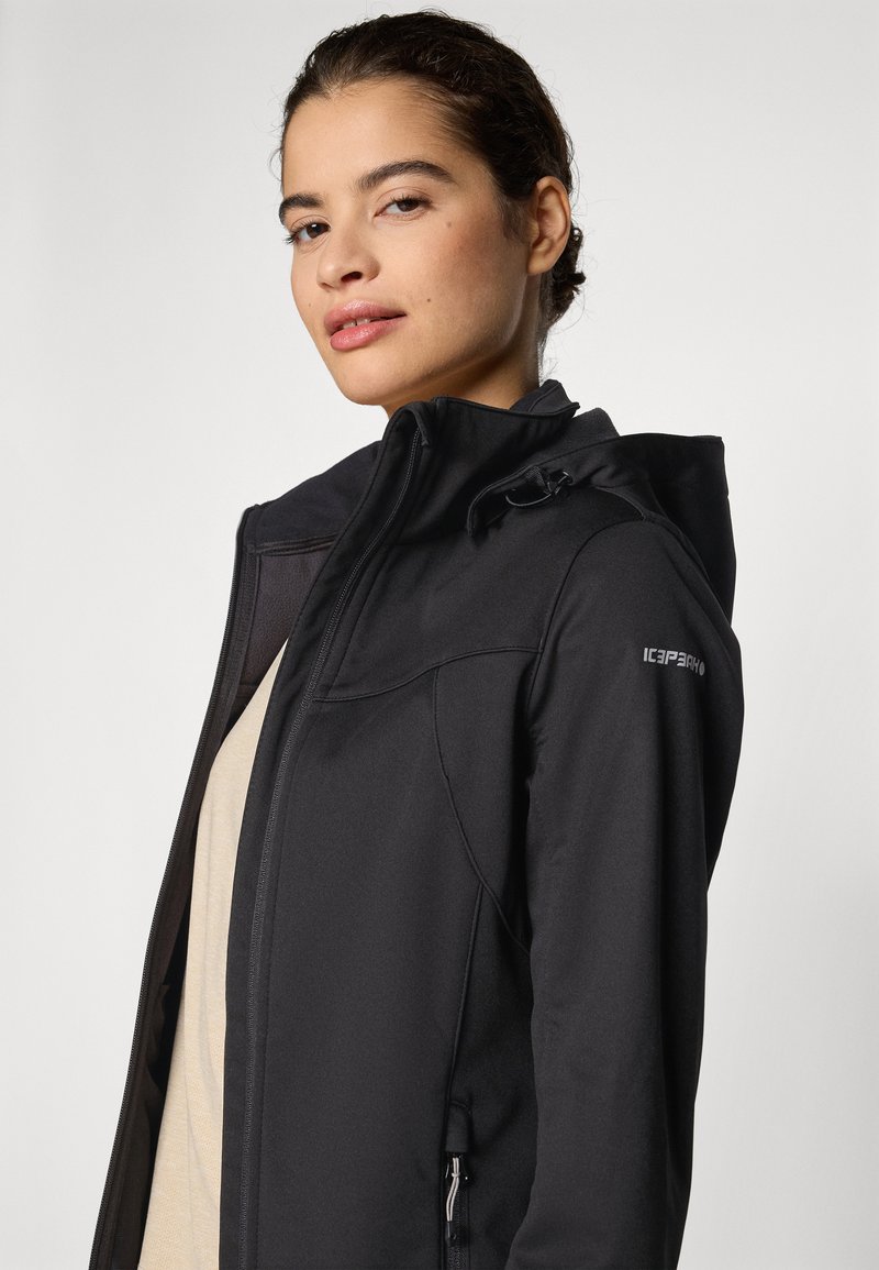 Chaqueta softshell negra con un alto cuello, cremallera frontal y capucha ajustable. Cuenta con bolsillos con cremallera y una textura suave.
