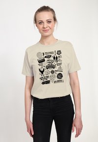 Hellbeiges Baumwoll-T-Shirt mit schwarzen grafischen Aufdrucken von Text und Symbolen, darunter ein Kassettenband, ein Auto und verschiedene Embleme.