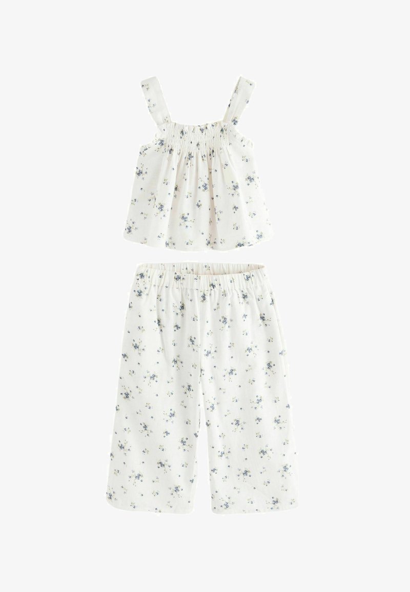 Vit blommig tvådelad set med en smockad tanktop med justerbara axelremmar och löst sittande, korta byxor dekorerade med små blå blommor.