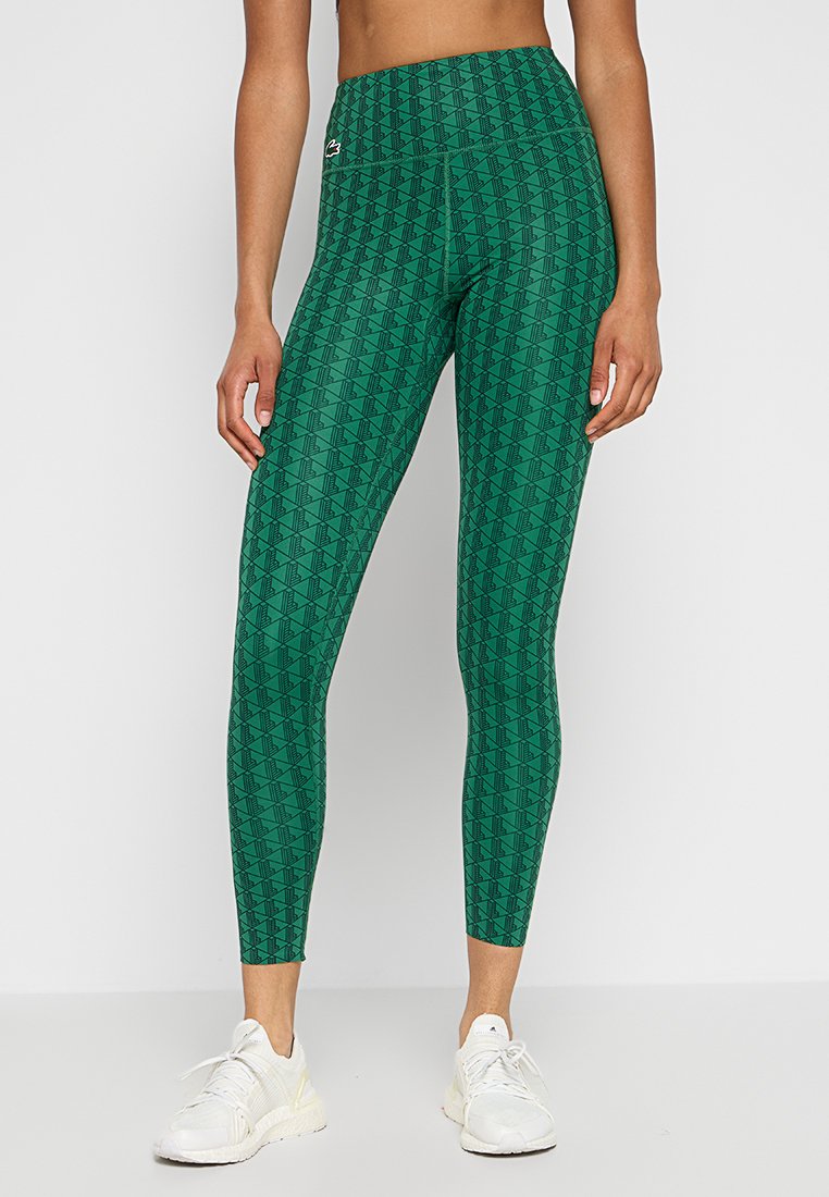 Leggings verdi con un motivo geometrico, design a vita alta, realizzati in materiale elasticizzato. Indossati con scarpe da ginnastica bianche.