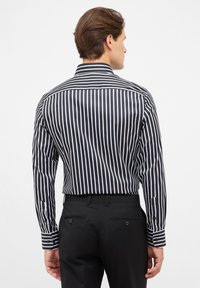 Zwart-wit gestreepte blouse met lange mouwen, knoopmanchetten, spitse kraag en een gladde textuur, gecombineerd met zwarte broeken.