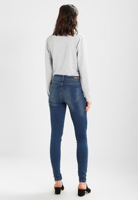 Tmavě modré džínové skinny džíny s vysokým pasem, se zadními kapsami a hladkou texturou. V kombinaci se šedým dlouhým rukávem a podpatky.