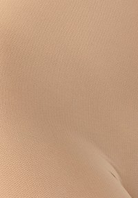 Acercamiento a una tela beige, finamente tejida, con un sutil patrón texturizado y un pequeño pliegue cerca de la esquina inferior derecha.