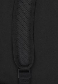 Svart tygrem med en vadderad, strukturerad yta med små perforeringar, säkrad med en svart metallklämma.