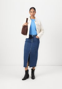 Jeanskjørt med frontspalte, parret med en lyseblå topp og en kremfarget jeansjakke. Brun skulderveske og sorte ankelstøvler fullfører looken.