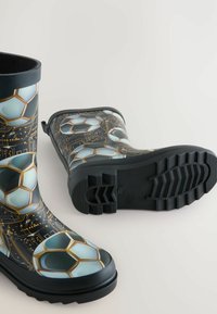 Bottes noires imperméables arborant un design graphique de ballons de football sur un fond de circuit imprimé, avec des semelles en caoutchouc texturé et des accents latéraux.