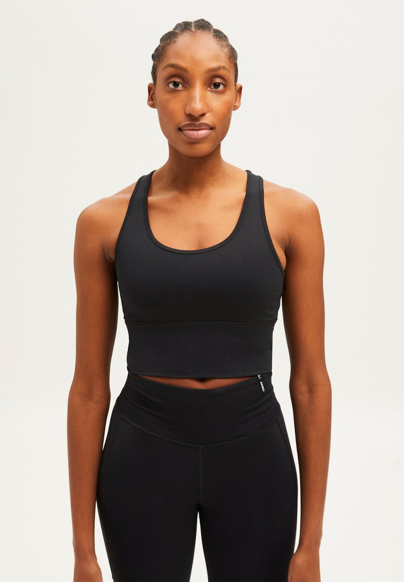 Zwarte sportieve crop top met een racerback ontwerp, met een gladde textuur en minimale stiksel. Gecombineerd met hoge zwarte leggings.
