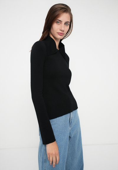 Svart langermet topp med krage, tettsittende design og ribbet tekstur. Brukt med lyseblå høytlivsjeans.