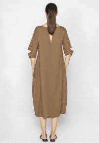 Brązowa midi sukienka z okrągłym dekoltem, krótkimi podwiniętymi rękawami oraz dekoltem typu łezka z tyłu. Wykonana z gładkiego materiału o luźnym fasonie.