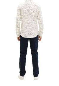 Chemise blanche avec des motifs verticaux noirs, manches longues et col boutonné, associée à un pantalon bleu foncé et des baskets blanches.