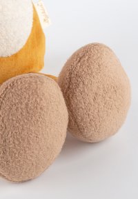 Jambes de jouet en peluche avec une texture douce et duveteuse ; couleur beige avec des formes arrondies. Le corps est jaune moutarde avec un détail circulaire blanc.