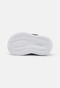 Czarne sneakersy z białą gumową podeszwą, charakteryzujące się teksturowanym wzorem antypoślizgowym. Projekt obejmuje gładką górę i minimalistyczne akcenty.
