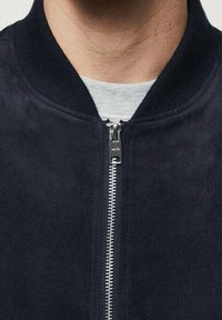 Giacca bomber blu navy con una texture liscia in suede, colletto a costine e chiusura frontale con cerniera argentata, dal design minimalista.