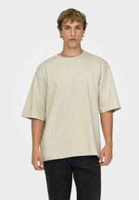 Beige oversized t-shirt lavet af blød bomuld. Har rund hals, korte ærmer og en afslappet pasform, kombineret med mørke jeans.
