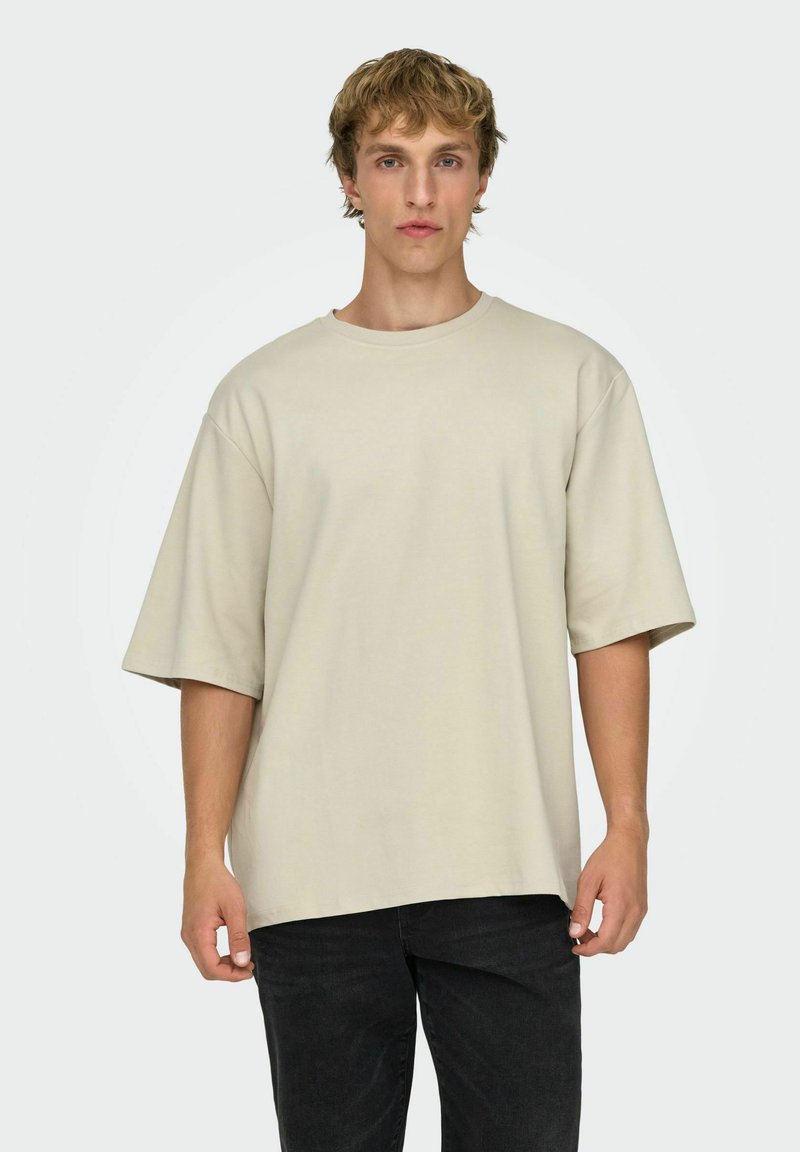 Beige oversized t-shirt lavet af blød bomuld. Har rund hals, korte ærmer og en afslappet pasform, kombineret med mørke jeans.
