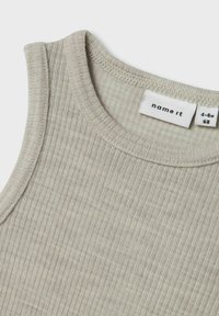 Débardeur beige à côtes avec un col rond et des bords cousus. L'étiquette indique "name it" avec une taille de 4-6 mois et des instructions d'entretien.