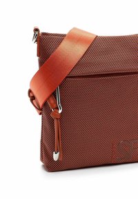 Sarkana austā auduma soma ar teksturētu virsmu, aprīkota ar regulējamu oranžu siksnu un sudrabotiem dekoratīviem elementiem, redzama sānu rāvējslēdzēja kabata.