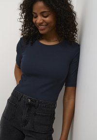 Haut à manches courtes côtelé navy associé à un jean noir taille haute avec poches avant et un détail de bouton en métal.