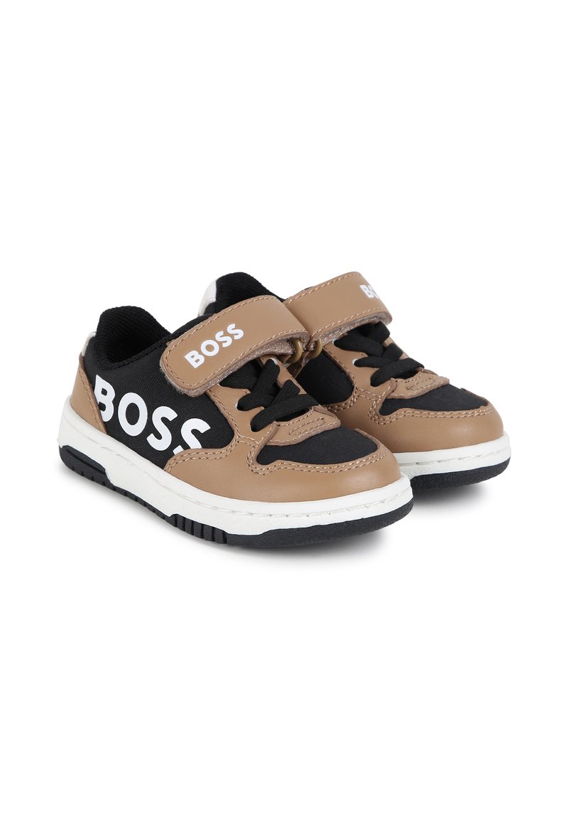 Zapatillas marrones y negras con correa de velcro y cordones, que cuentan con un logo blanco en el costado, suela de goma y acentos de cuero texturizado.