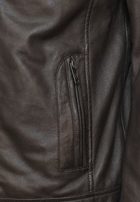 Bruine leren jacksectie met een zichtbare ritssluiting, een gladde textuur en nette stiksels langs de naden.