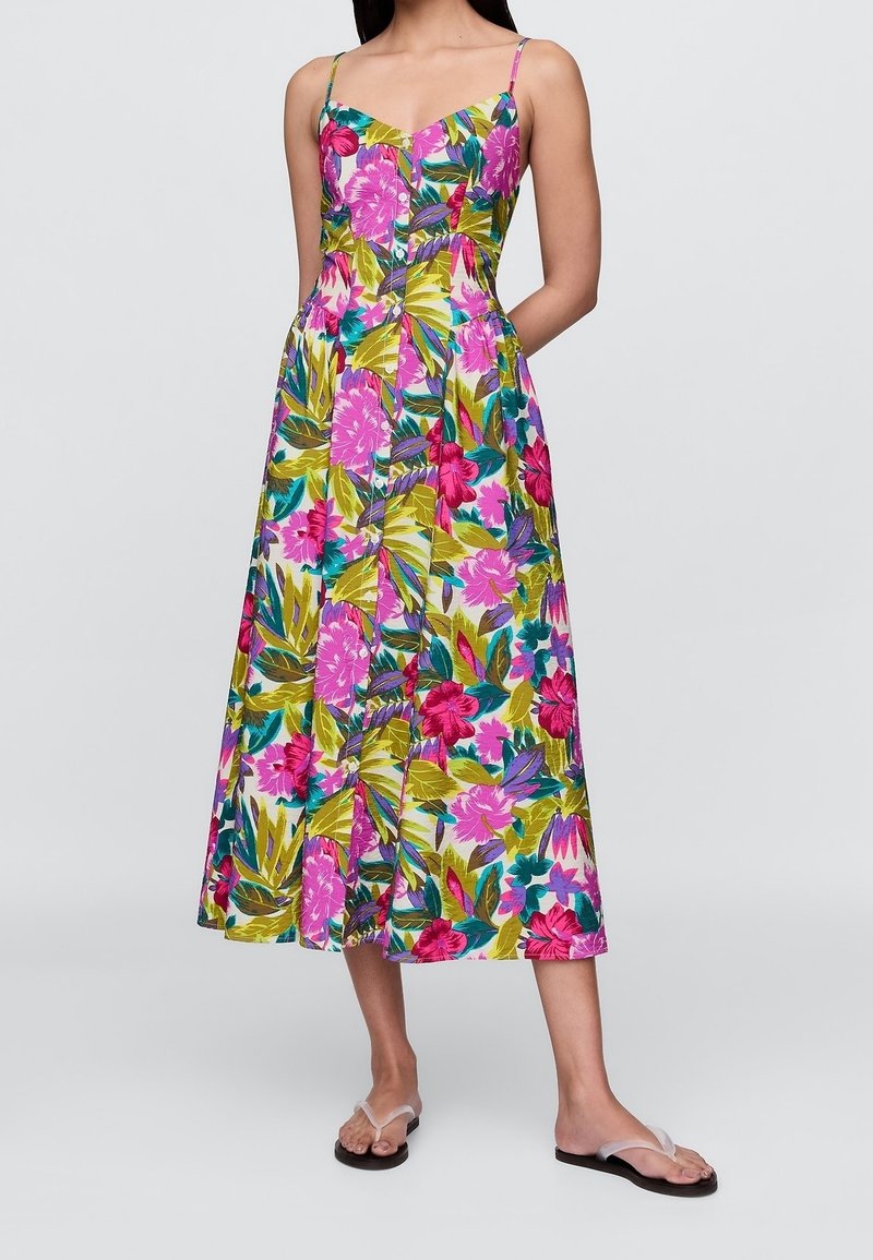 Femme portant une robe midi sans manches boutonnée avec un imprimé floral tropical coloré et de fines bretelles, assortie à des sandales à brides transparentes.