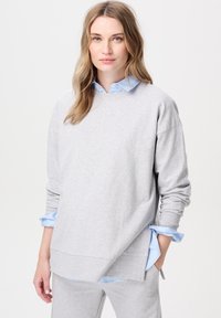Hellgrauer Pullover aus weichem Material mit Rundhalsausschnitt und überschnittenen Schultern, über einem hellblauen Hemd mit Kragen getragen.