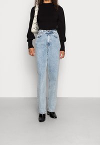 Zwarte geribbelde trui met lange mouwen en opgezette schouders, gecombineerd met lichtblauwe high-waist rechte jeans en zwarte enkellaarzen.