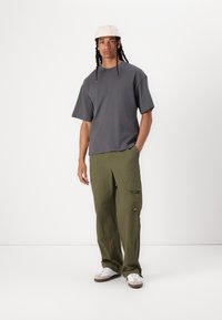 Grey oversized t-shirt, olive green baggy cargo pants with pockets, and white sneakers. Model wears a light-colored cap. Simple design and relaxed fit.