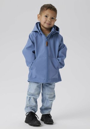 Veste à capuche bleue avec une fermeture éclair à l'avant, deux poches et une texture lisse. Associée à un pantalon cargo bleu clair et des baskets noires.