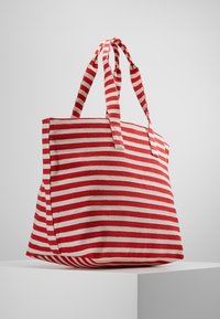 Sac fourre-tout rayé en rouge et beige, fabriqué en toile, avec deux poignées robustes et un corps large et structuré.