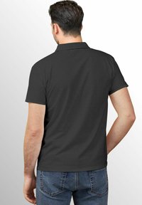 Schwarzes Polo-Shirt mit Kragen, kurzen Ärmeln und glatter Textur; getragen mit blauen Jeans, die ein einfaches Design haben und keine sichtbaren Logos aufweisen.
