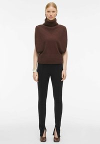 Brun strikket turtleneck-sweater med puffede ærmer, parret med sorte, tætsiddende bukser med slids ved anklerne og brune hæle.