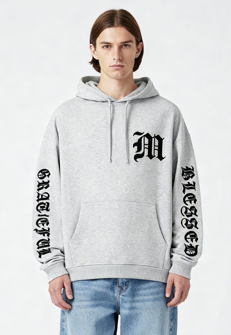 Felpa grigia in pile con tasca a marsupio. Presenta la stampa nera della scritta "M" e "GRATEFUL" sulle maniche e "BLESSED" sul petto.