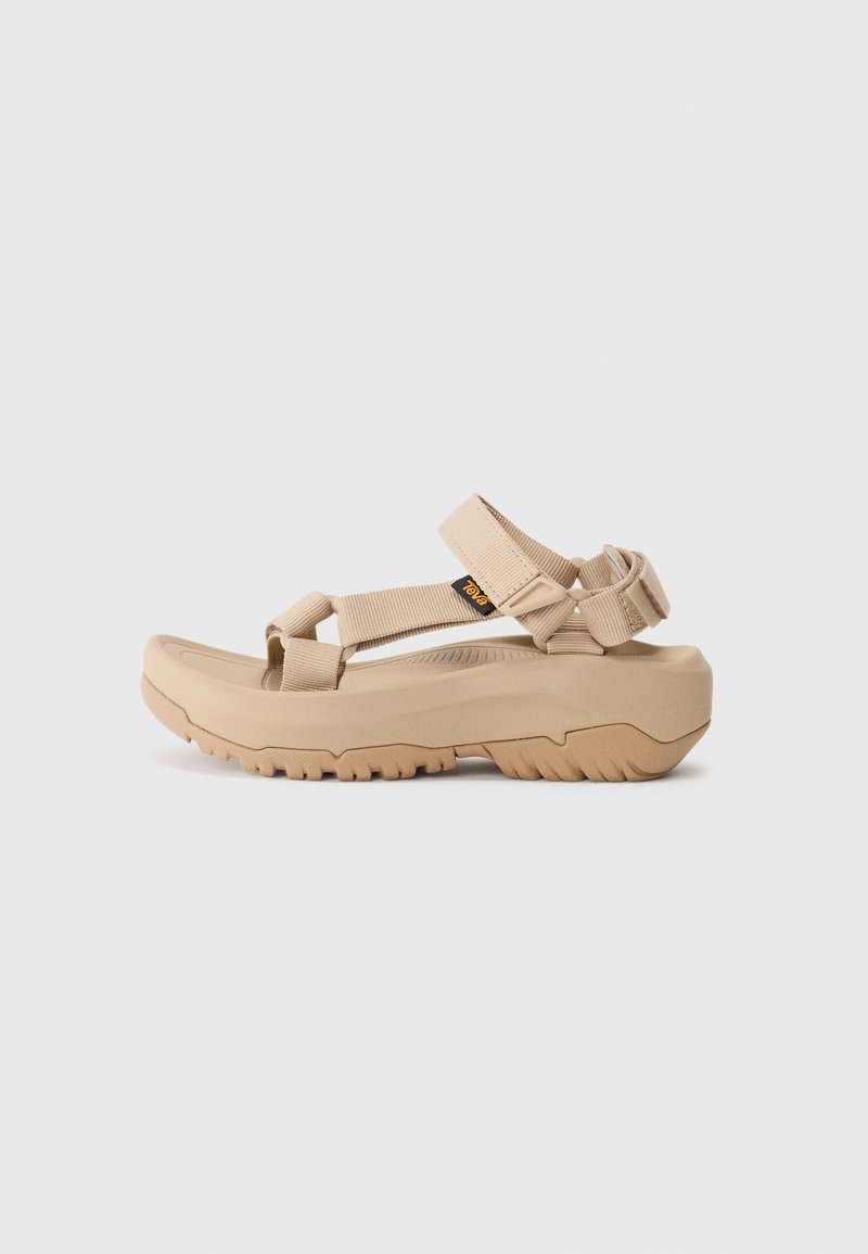 Light beige sandals featuring a molded footbed, adjustable straps, and a textured rubber sole for grip. Simple design with minimal accents.