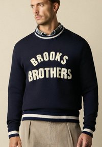 Námořnický vlněný svetr s nápisem "BROOKS BROTHERS" v krémové barvě. Má žebrované manžety a lem s bílými a námořnickými pruhy.
