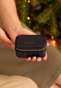 Rektanguläre schwarze Krokodilledertasche mit goldenem Reißverschluss, in einer Hand gehalten, auf einer neutralen Oberfläche platziert.