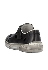 Schwarzer Lederschuh mit Ausschnitten und Klettverschluss, strukturierten Gummisohle und silbernen Akzenten. Markenlogo sichtbar an der Ferse.