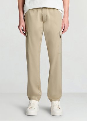 Pantaloni cargo beige con fronte piatto, vita elastica, tasche laterali e gambe dritte, abbinati a sneakers bianche. Tessuto dalla texture liscia.