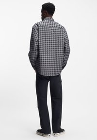 Harmaa-musta ruudullinen kauluksellinen paita, jossa on takakappale, kaareva helma ja pitkät hihat, yhdistetty tummiin cargo-housuihin ja lenkkareihin.