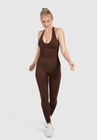 Bruine, rekbare bodysuit met halternek ontwerp en een aansluitende silhouet, aangevuld met witte sportschoenen.