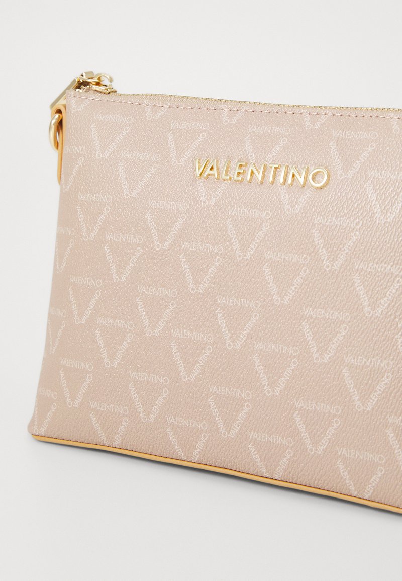 Pochette synthétique beige avec motif de logo embossé, quincaillerie dorée et fermeture éclair. Dotée d'une texture lisse et de coutures jaunes contrastantes.