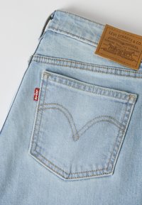 Poche arrière de jean en denim bleu clair avec l’étiquette rouge Levi’s et un patch en cuir marron de la marque Levi Strauss & Co. au-dessus de la ceinture.