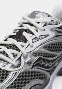 Primo piano di una scarpa da corsa Saucony grigia e bianca con tessuto a rete, lacci bianchi e dettagli del logo in nero e argento.