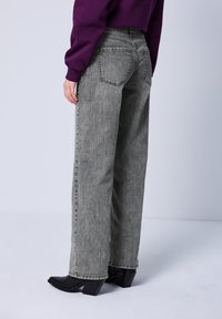 Hoch taillierte, l�ässig geschnittene Jeans aus verblasstem grauem Denim; verfügt über ein klassisches Fünf-Taschen-Design und sichtbare Nähte. Kombiniert mit schwarzen Absatzstiefeln.