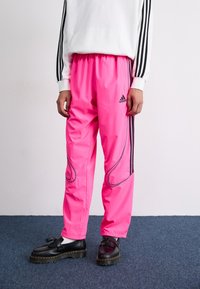 Bright pink athletic pants with black side stripes and grey accents, featuring an elastic waistband and loose-fit design.