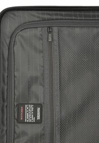 Black zippered travel bag interior with mesh pockets, textured fabric, and thin vertical stripes. Includes a manufacturer's label.