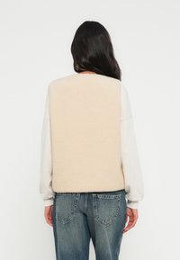 Πίσω πάνελ με επένδυση από φλίς σε απαλή μπεζ απόχρωση, σε συνδυασμό με ανοιχτό γκρι φούτερ. Χαλαρή εφαρμογή με ριμπ μανσέτες στα μανίκια και κανονικά τζιν παντελόνια.